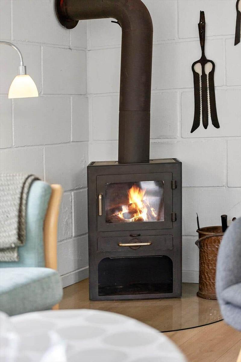 Holzofen mit brennendem Feuer in einem Raum mit weißen Ziegelwänden und Sitzgelegenheiten.