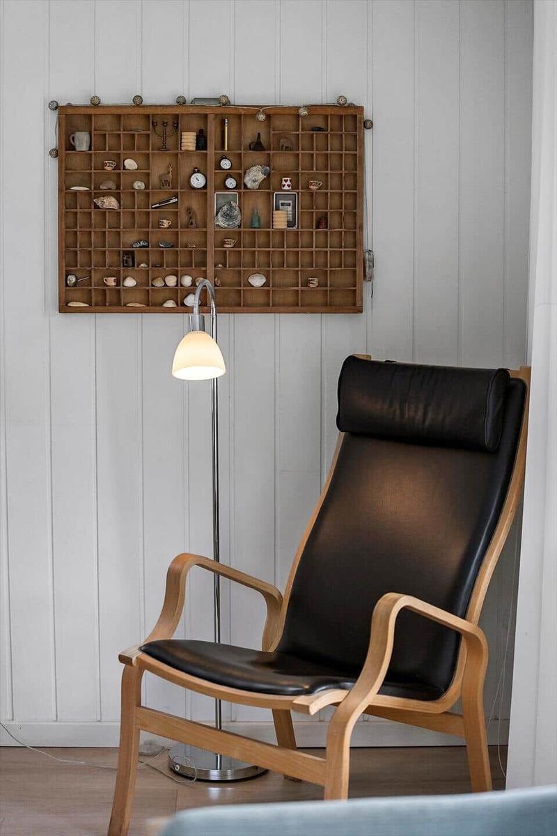 Schwarzer Ledersessel vor Holzregal mit Sammlerobjekten an weißen Wänden.