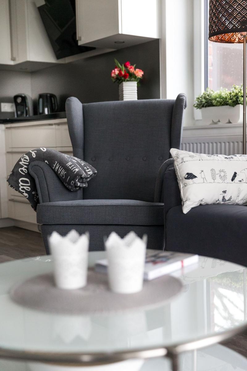 Ein grauer Sessel mit Kissen und Decke vor einem Fenster.