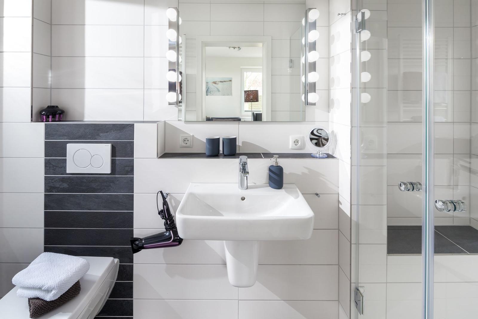 Badezimmer mit Waschbecken, Spiegel und Dusche. Schwarze und weiße Fliesen.