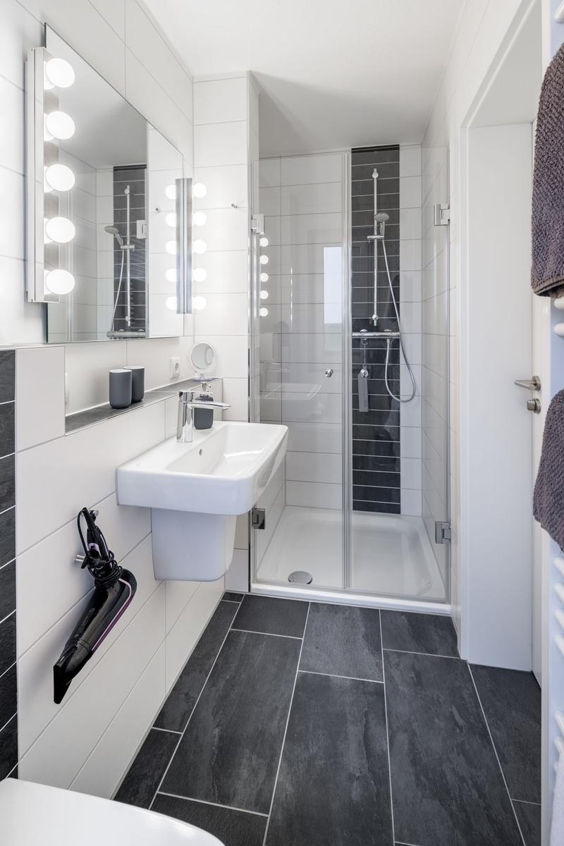 Badezimmer mit Dusche, Waschbecken und beleuchtetem Spiegel.
