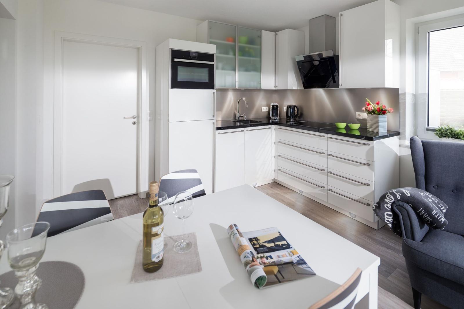 Moderne Küche mit Essbereich und Sitzgelegenheit. Weiße Schränke, schwarze Arbeitsplatten.