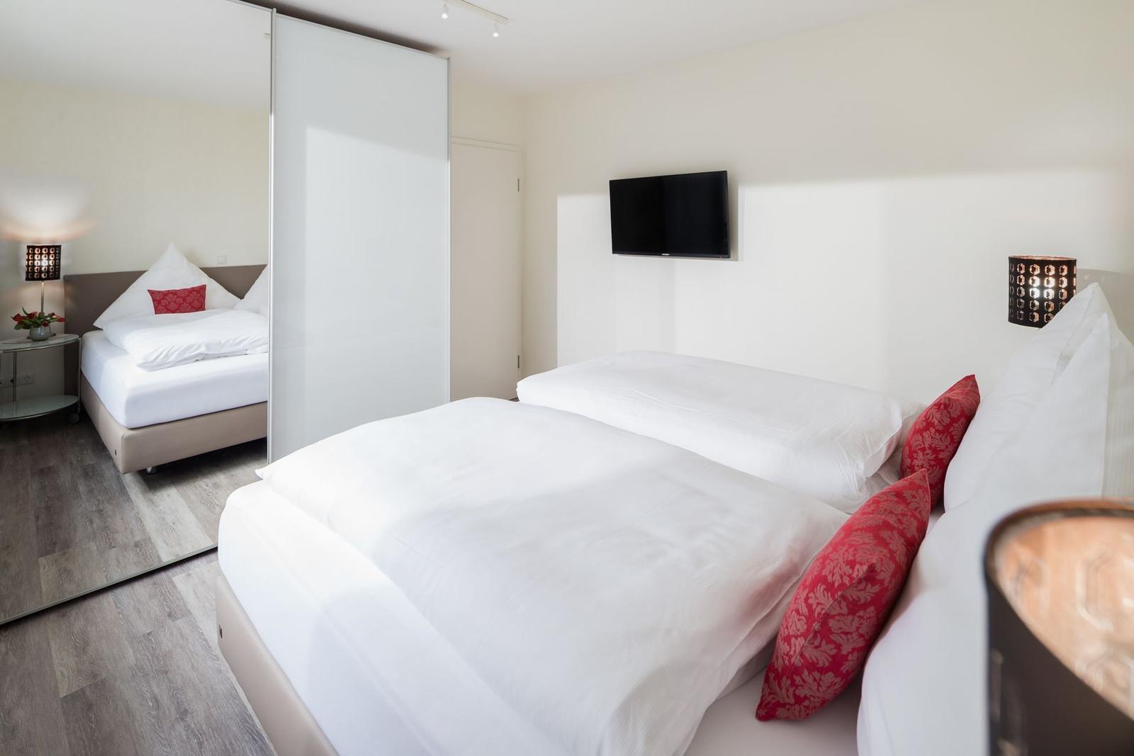 Schlafzimmer mit Doppelbett, Spiegelschrank und Wandfernseher.