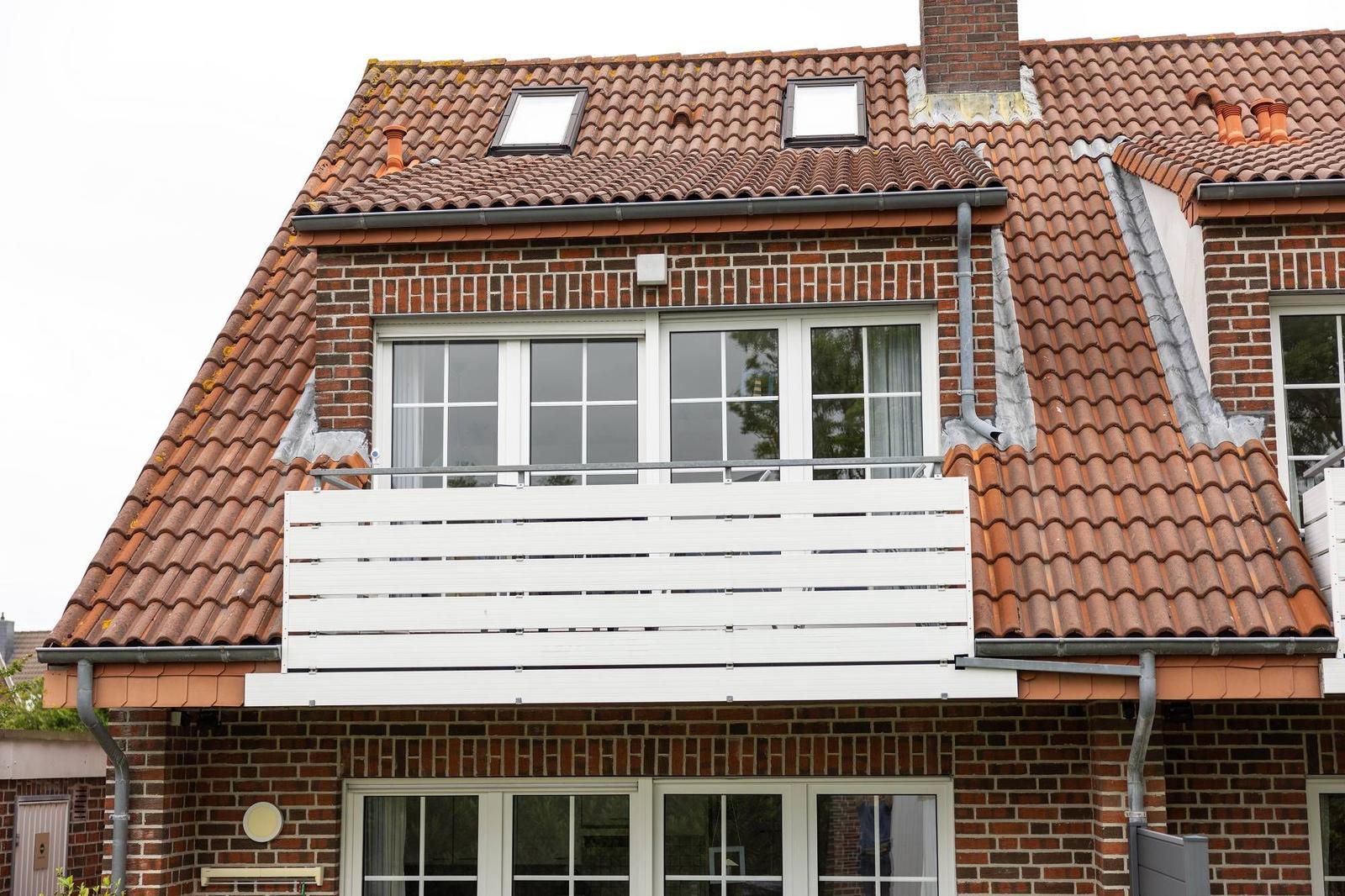 Haus mit rotem Ziegeldach, weißen Fenstern und Balkon