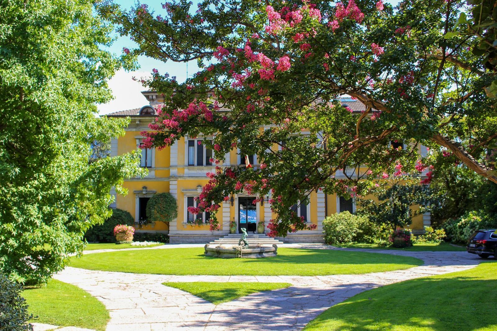 A yellow villa with garden, fountain, and flowering trees.
