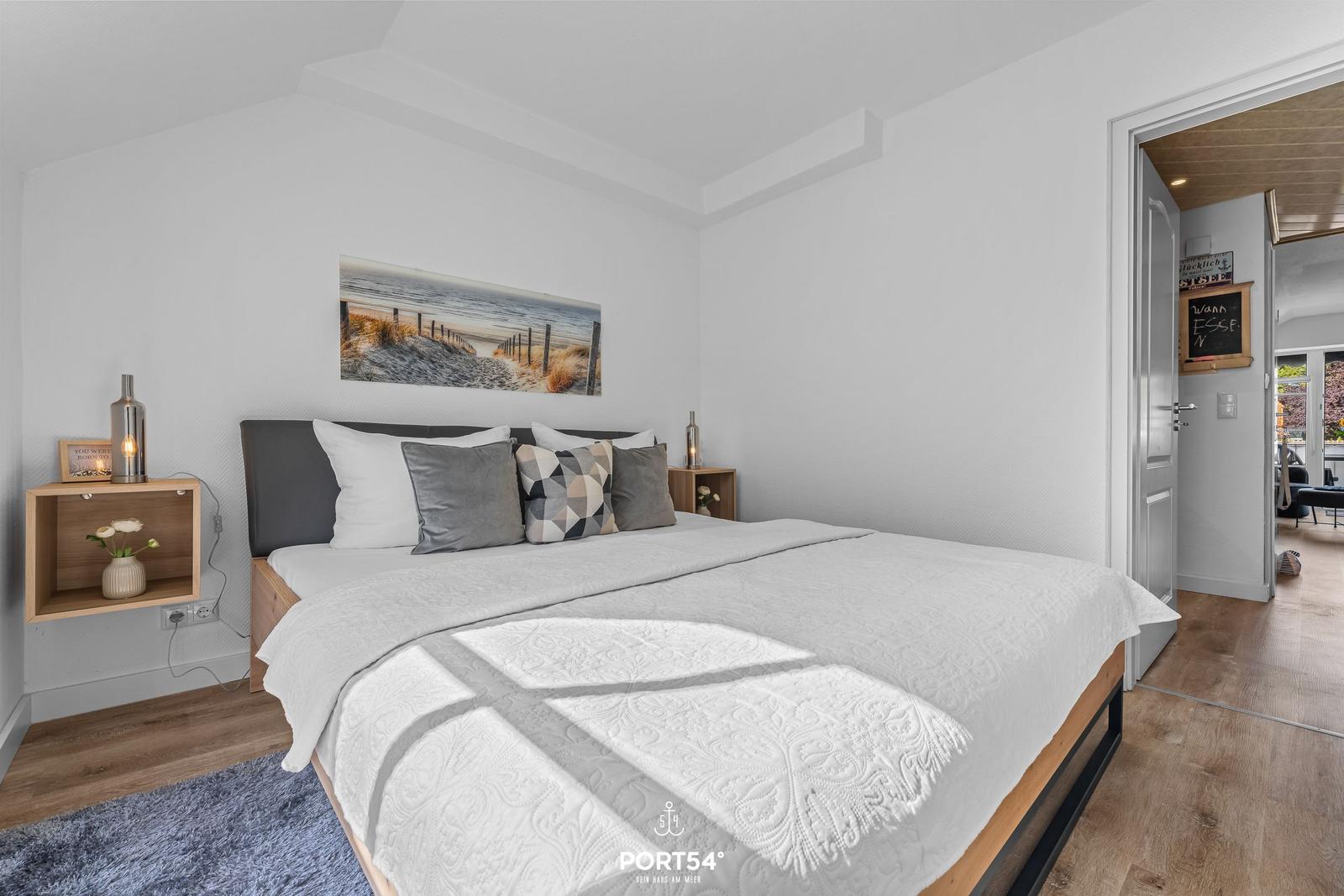 Schlafzimmer mit Bett, Wandbild und Nachttischen.