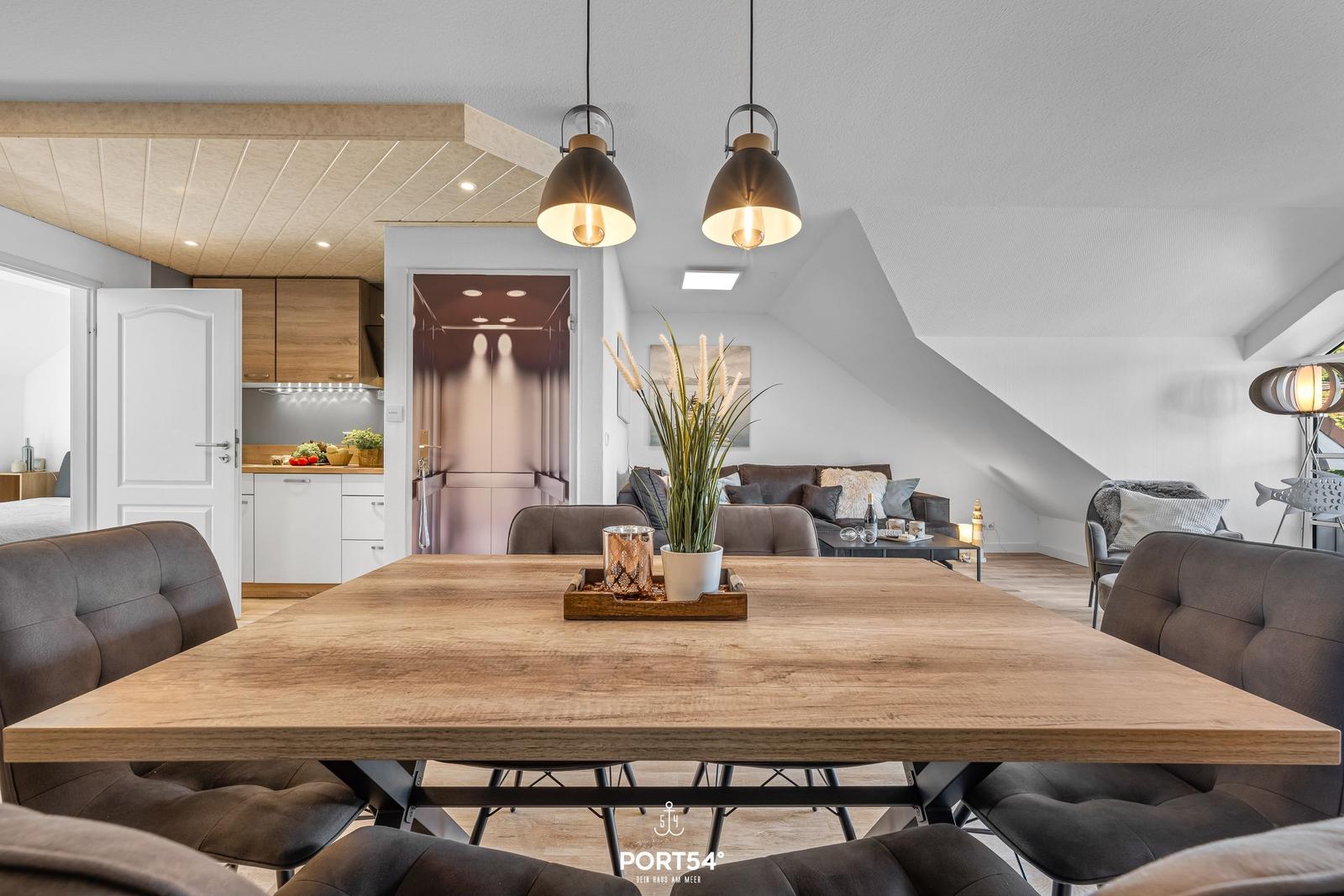 Essbereich mit Holztisch und dunklen Sitzgelegenheiten. Küche und Wohnzimmer sind sichtbar.