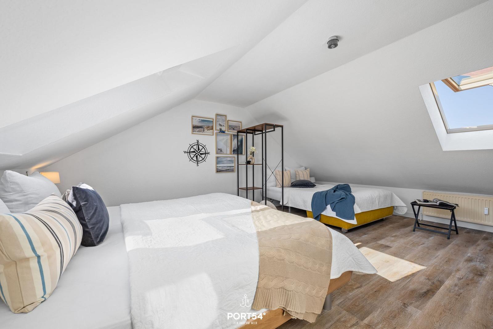 Zwei Betten unter Dachschrägen mit Fenster und Wanddekoration.