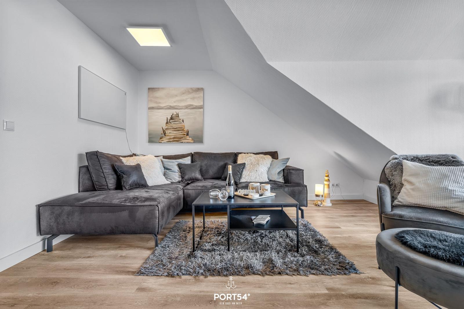 Wohnzimmer mit grauem Sofa, Couchtisch und Wandbild unter Dachschräge.