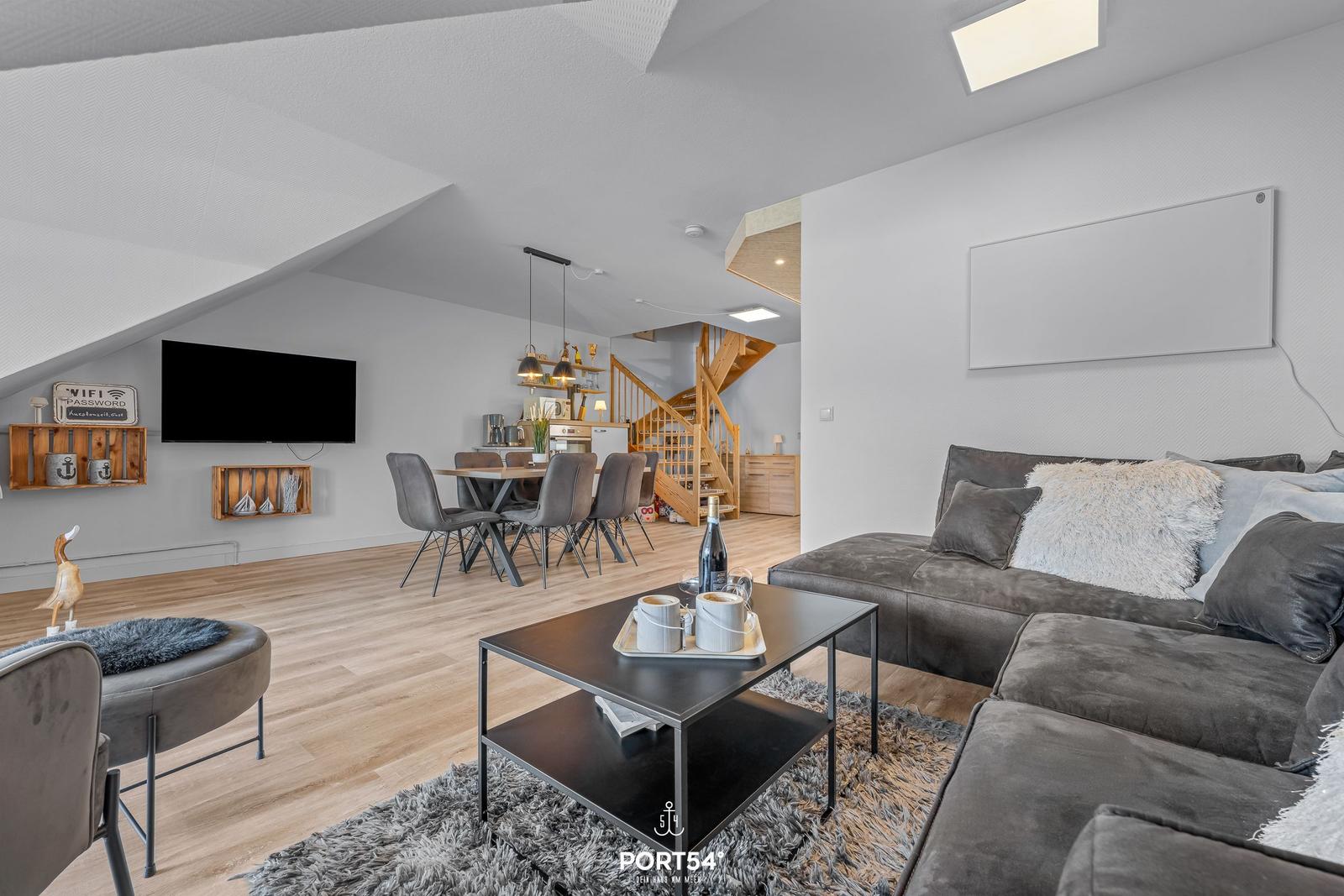 Wohn- und Essbereich mit Sofa, Couchtisch und Fernseher unter schrägen Dachdecken.