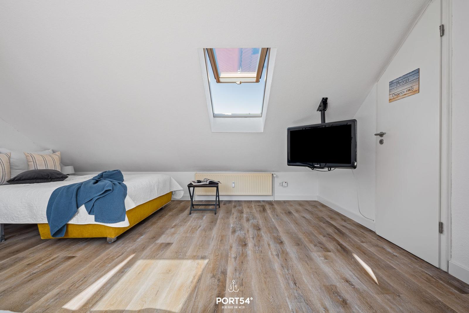 Schlafzimmer mit Dachschräge, Dachfenster, Bett und Wand-TV.