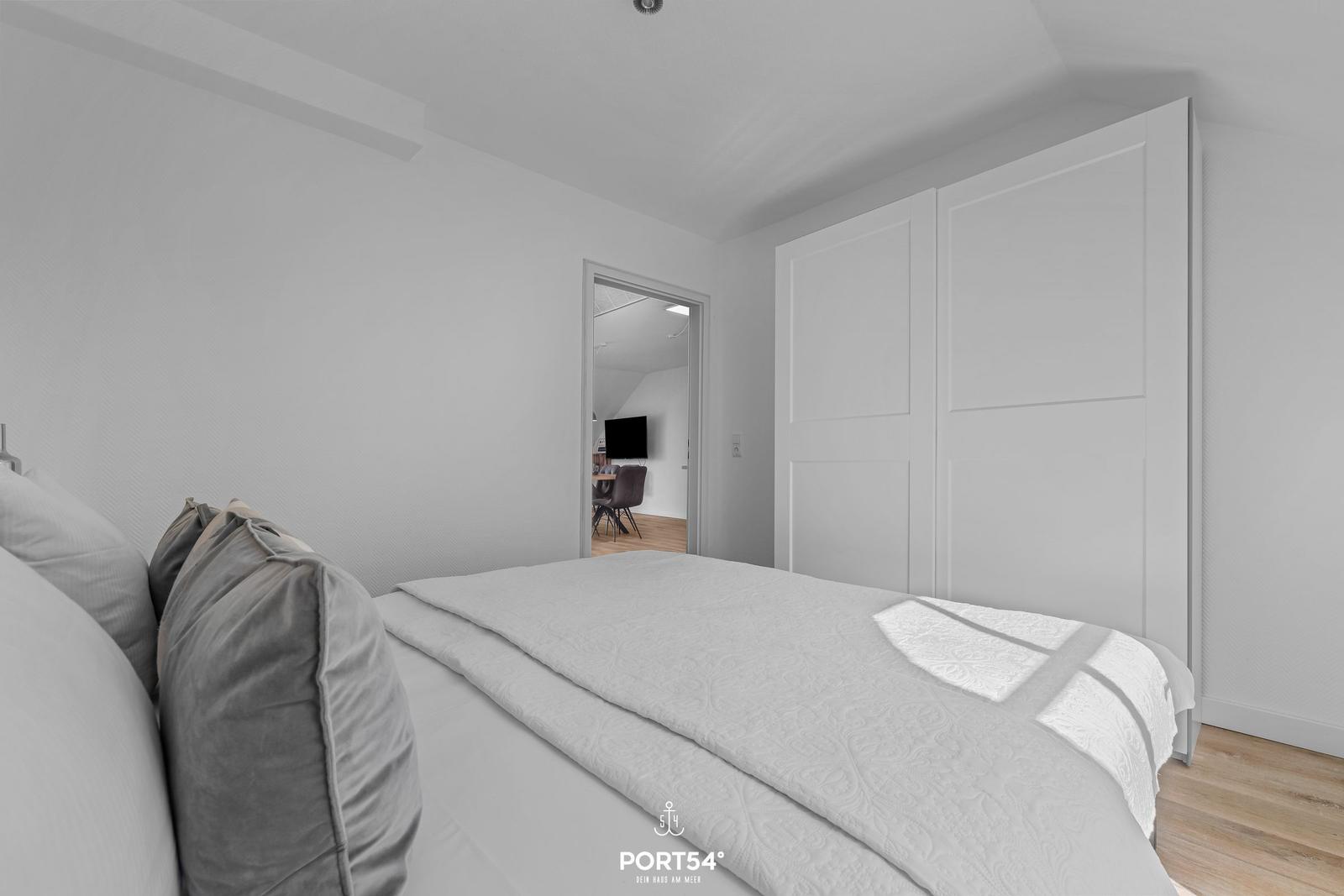 Schlafzimmer mit Bett, Kleiderschrank und Blick in Wohnbereich.