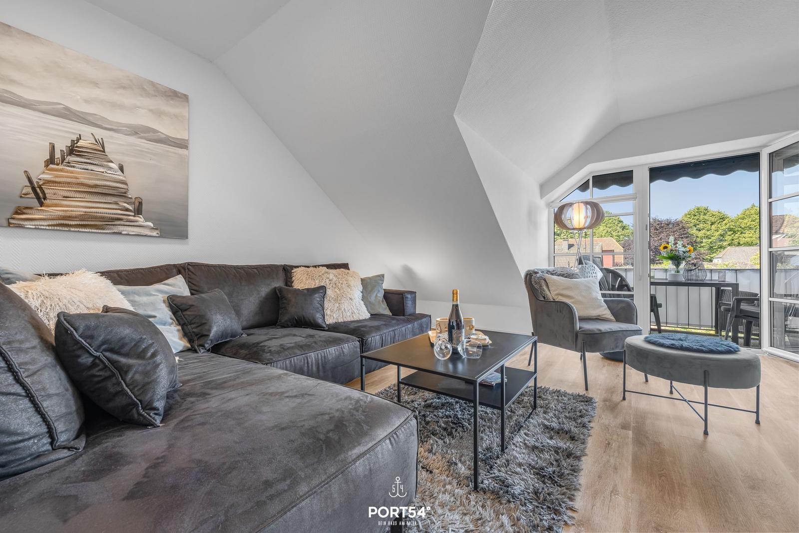 Wohnzimmer mit Sofa, Sessel und Balkonzugang