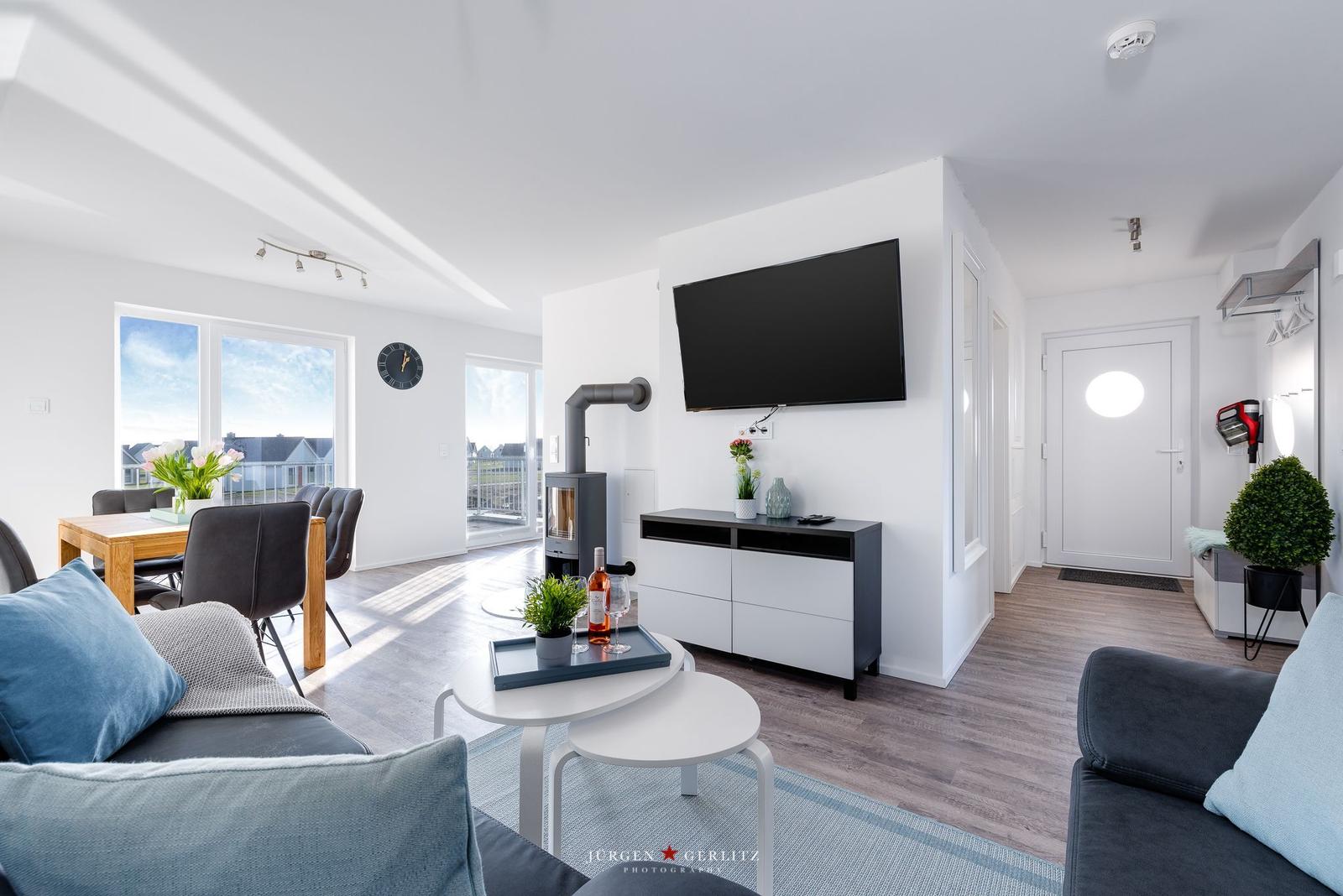 Wohnbereich mit Sofa, TV, Esstisch und Blick auf Balkon.