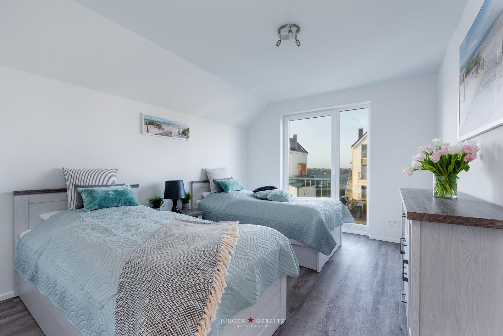 Zwei Betten mit hellblauen Bettwäschen und einem Balkon mit Blick.