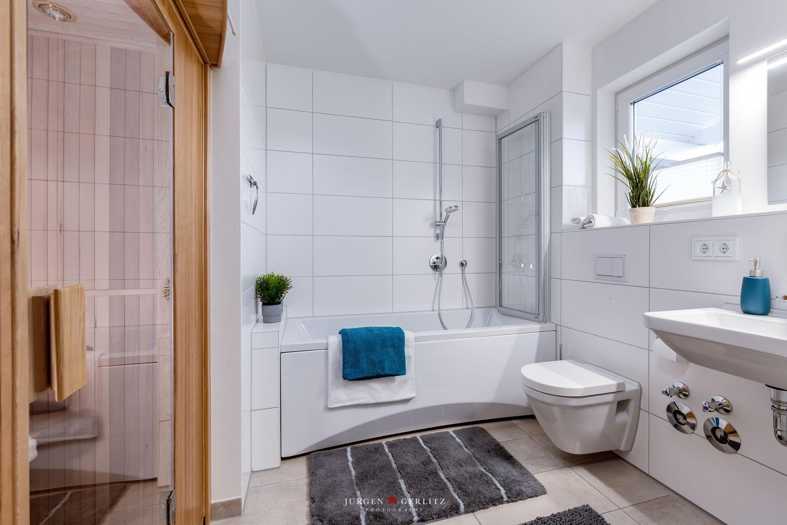 Badezimmer mit Badewanne, Dusche und Waschbecken. Fenster mit Pflanze.