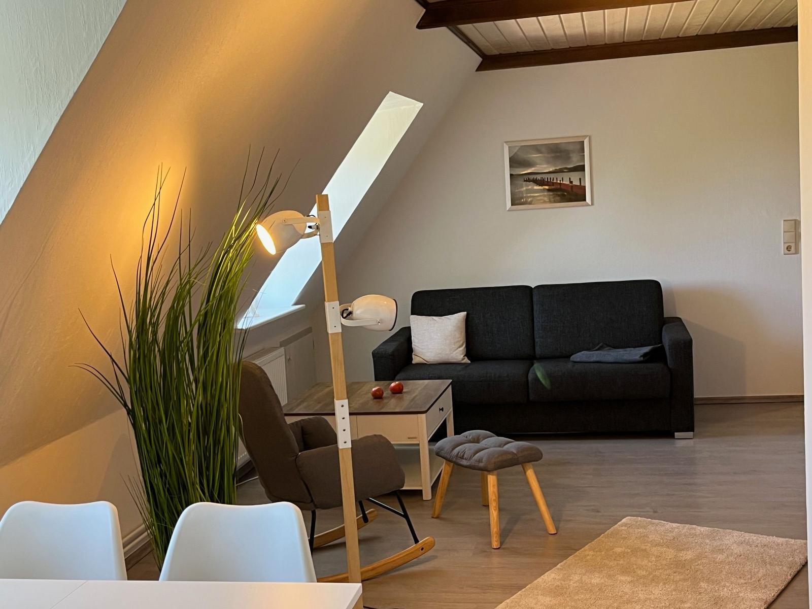 Wohnzimmer mit Sofa, Stehlampe und Pflanze unter Dachschrägen.