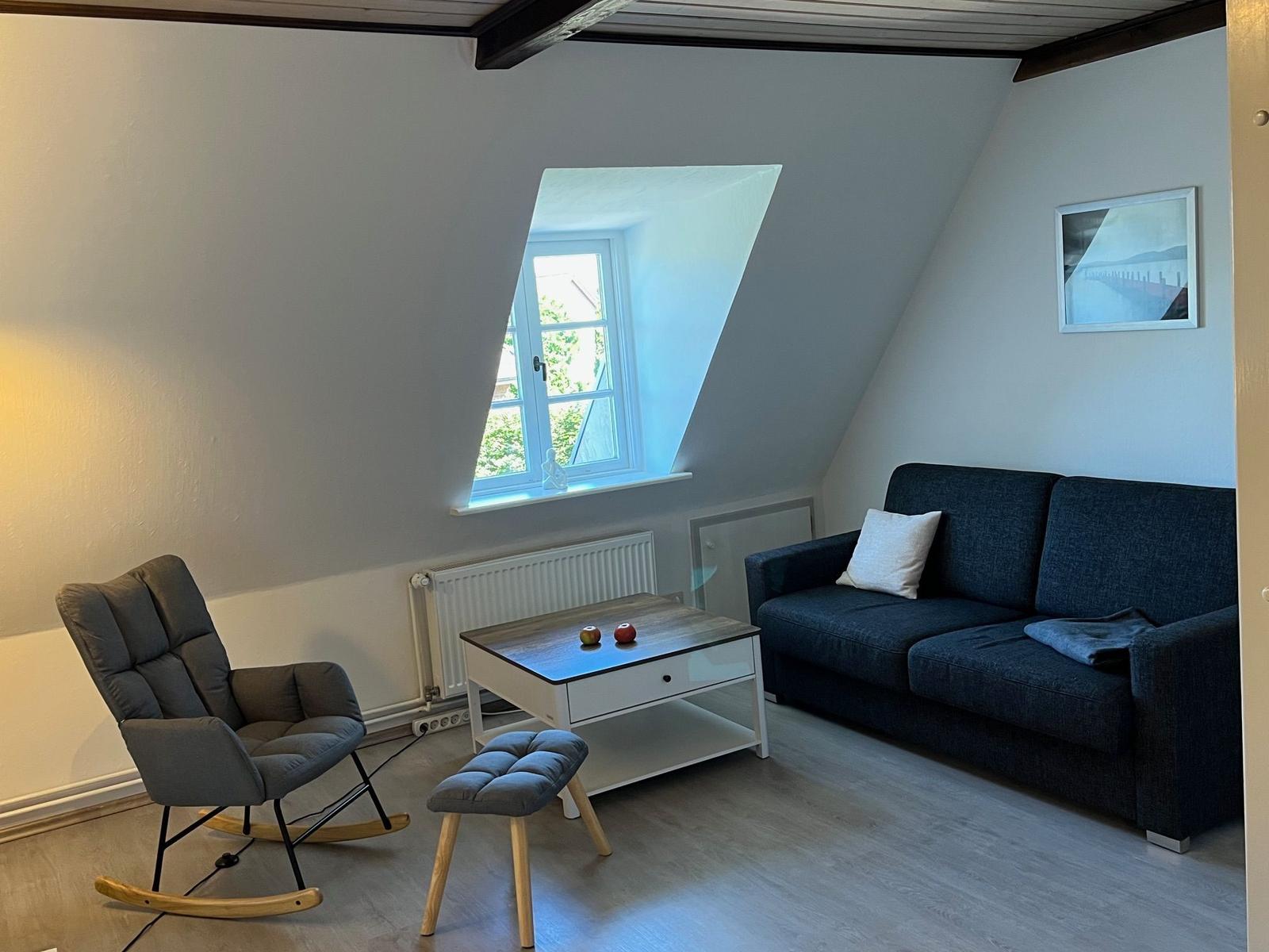 Wohnzimmer mit Sofa, Sessel und Dachfenster.
