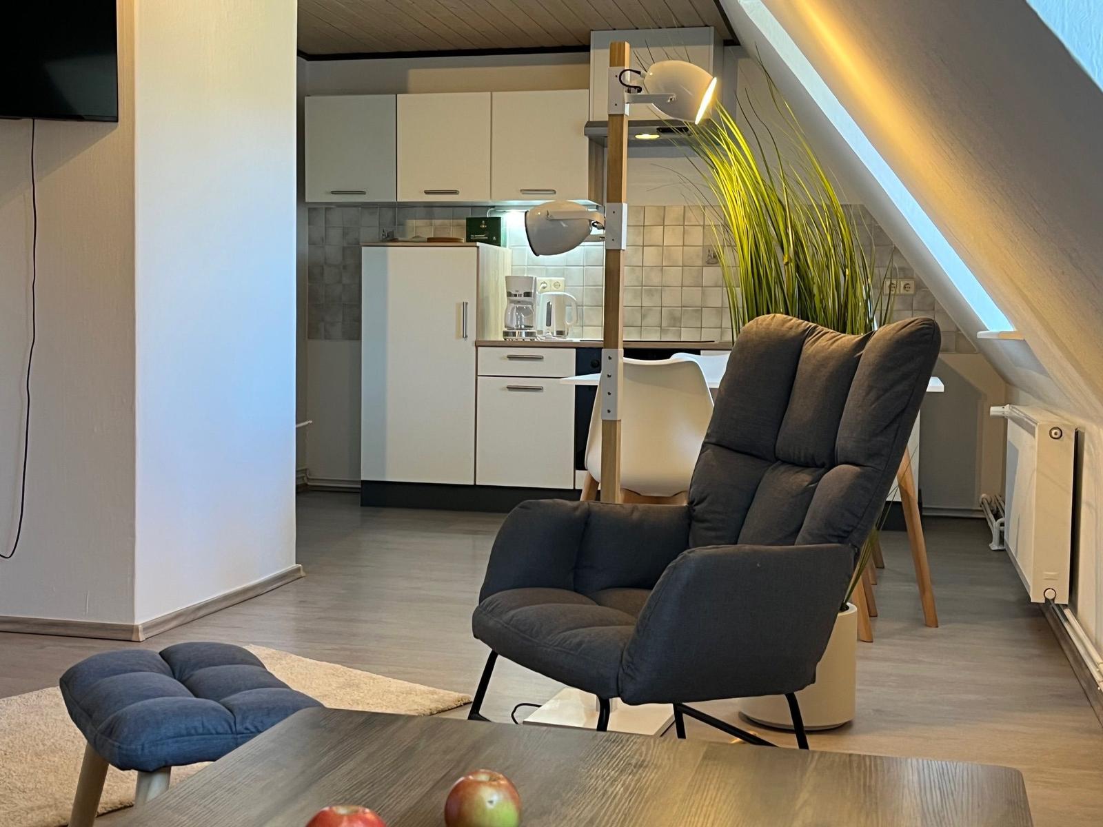 Ein Wohnzimmer mit Sessel, Küchenbereich und Dachschrägen.