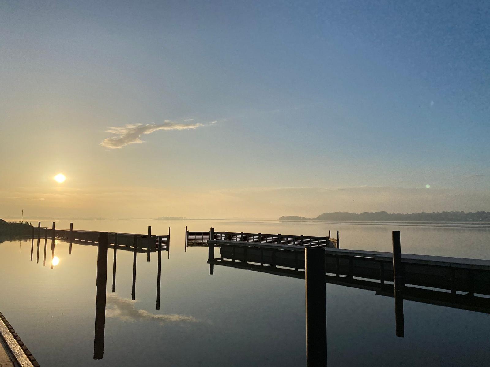 Sonnenuntergang über ruhigem Wasser mit Holzsteg im Vordergrund.