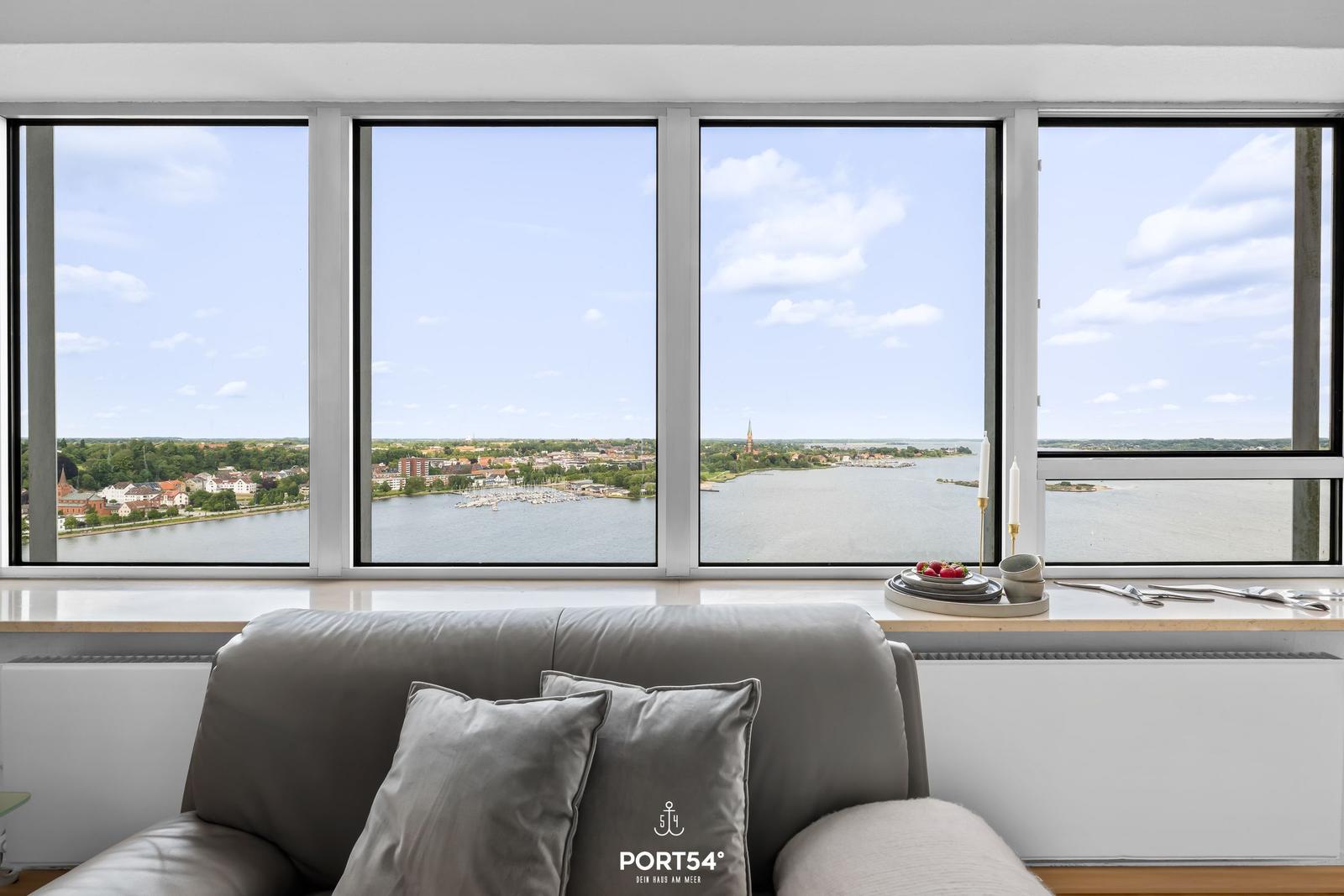 Sofa mit Kissen vor großem Fenster mit Blick auf Wasser und Stadt