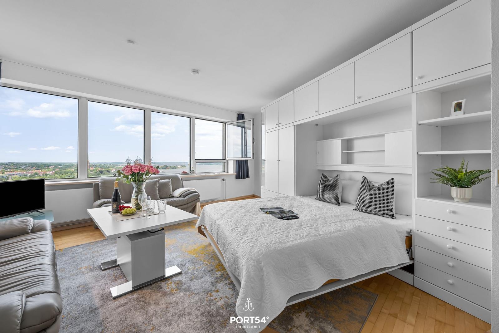 Ein Raum mit Bett, Sofa und großem Fenster mit Blick auf die Landschaft.