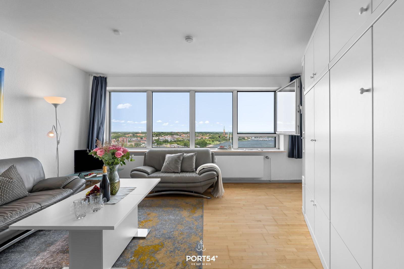 Wohnzimmer mit Blick auf Fluss und Stadt. Sofa, Couchtisch und Kleiderschrank.