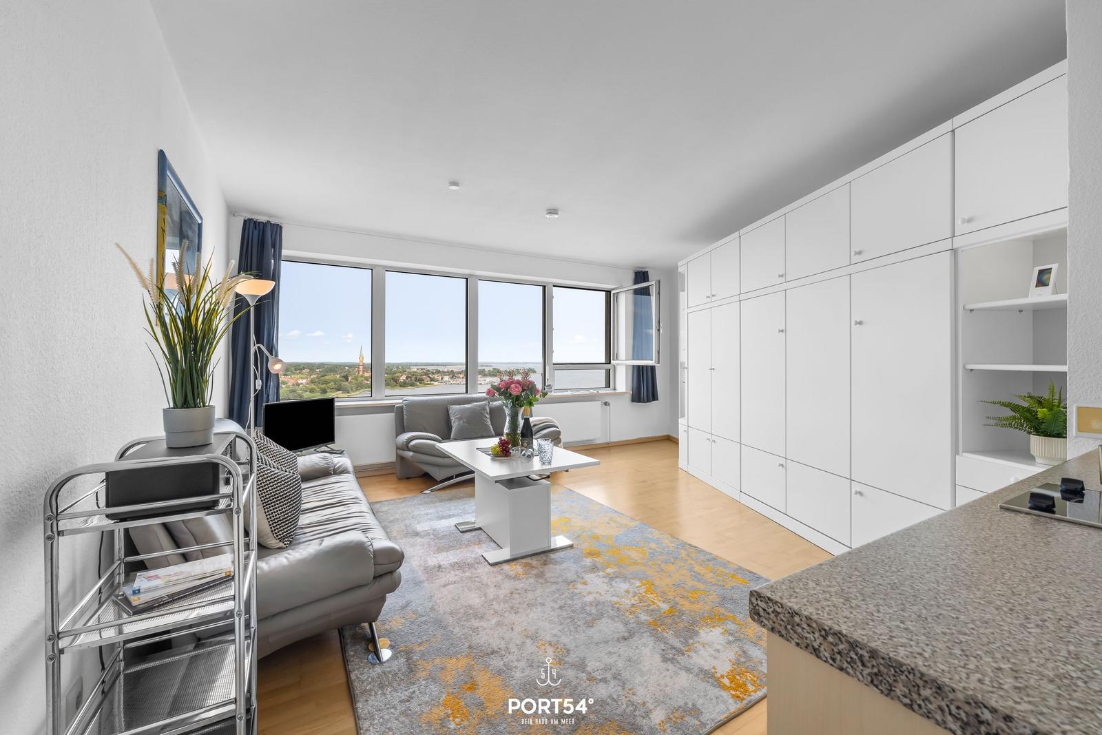 Wohnbereich mit großem Fenster, Sofa, Couchtisch und weißen Schränken.