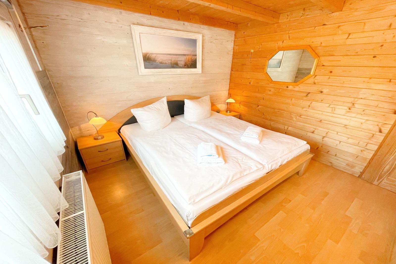 Schlafzimmer mit Holzwand, Bett, Nachttisch und Spiegel