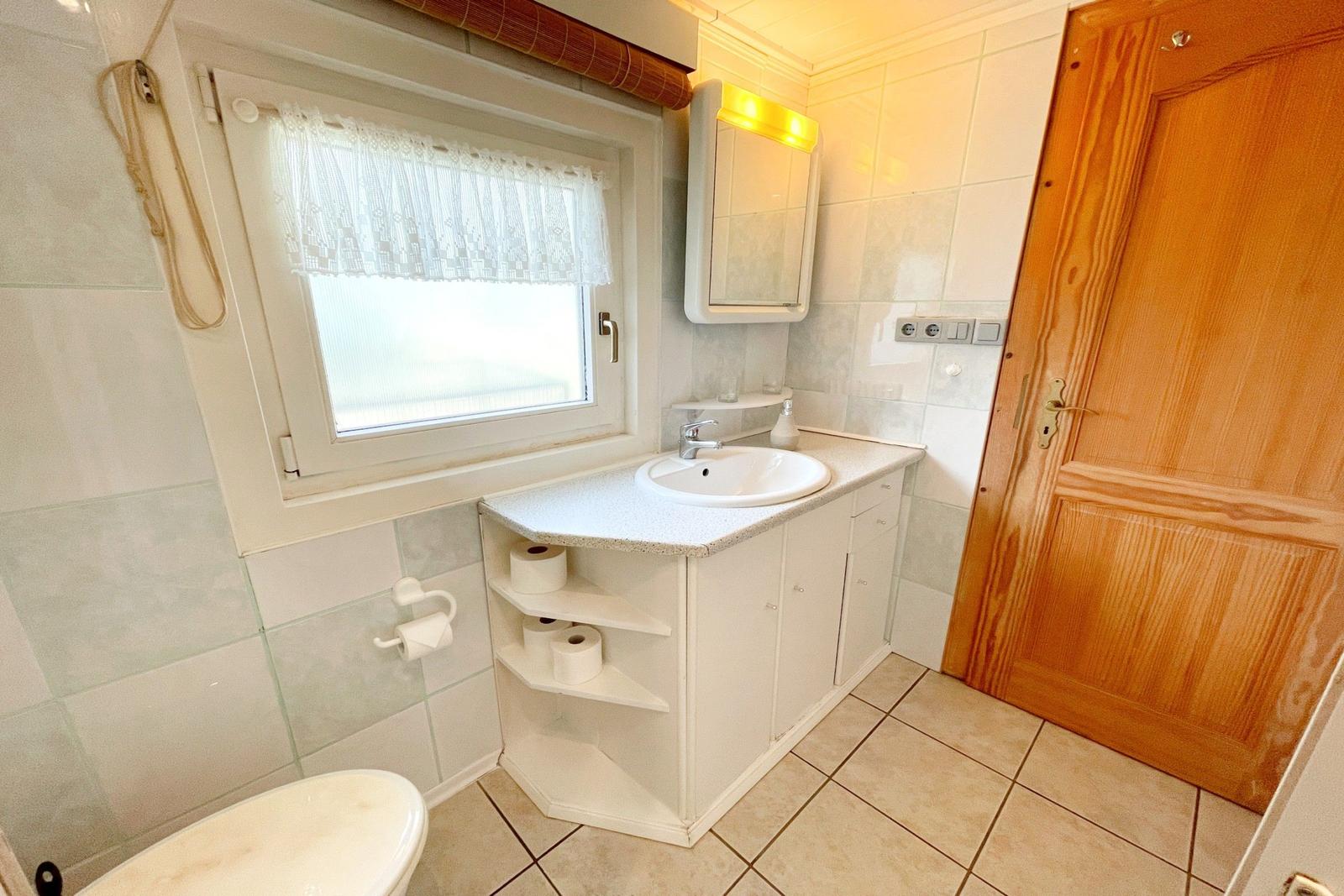 Badezimmer mit Waschbecken, Spiegel, Toilette und Fenster mit Vorhang.