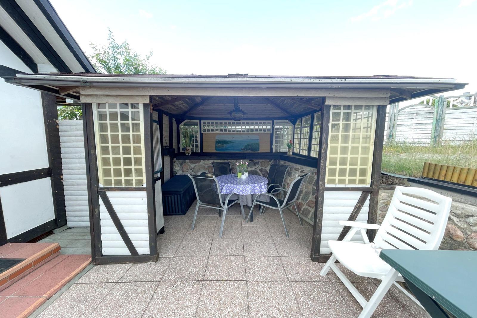 Terrasse mit Pavillon, Tisch, Stühlen und Steinwand. Weiße Gartenstühle und Tisch sind ebenfalls vorhanden.