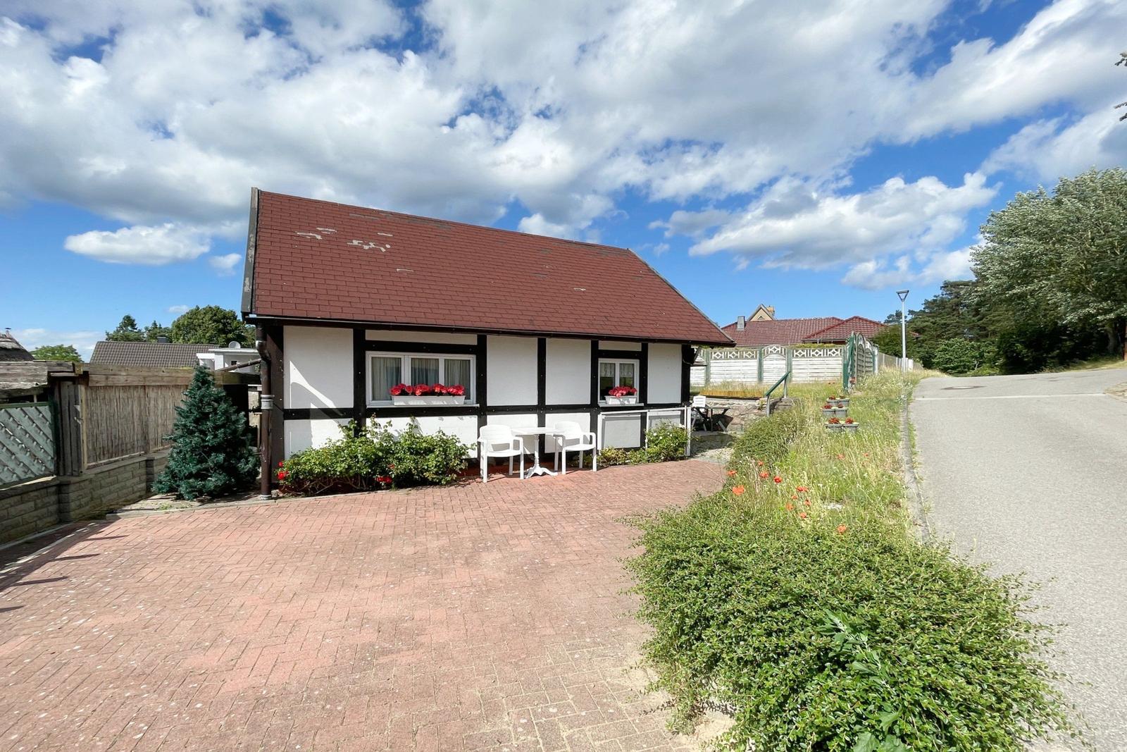 Haus mit Terrasse, Garten und rotem Ziegeldach unter blauem Himmel.
