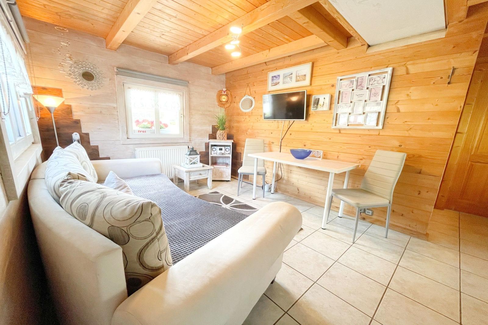 Wohnraum mit Sofa, Tisch und Fernseher an Holzwand