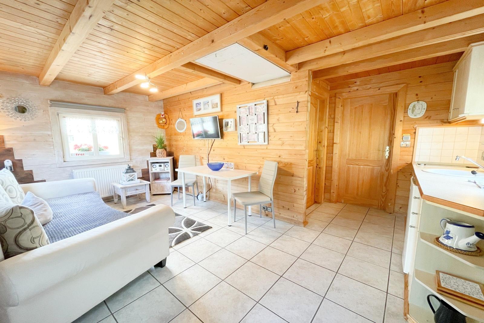 Wohnküche mit Holzwand, Sofa, Esstisch und Küchenzeile.