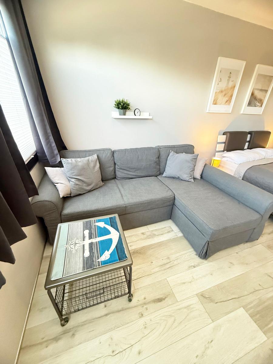 Ein Wohnbereich mit grauem Sofa, Tisch mit Ankern und Bett im Hintergrund.