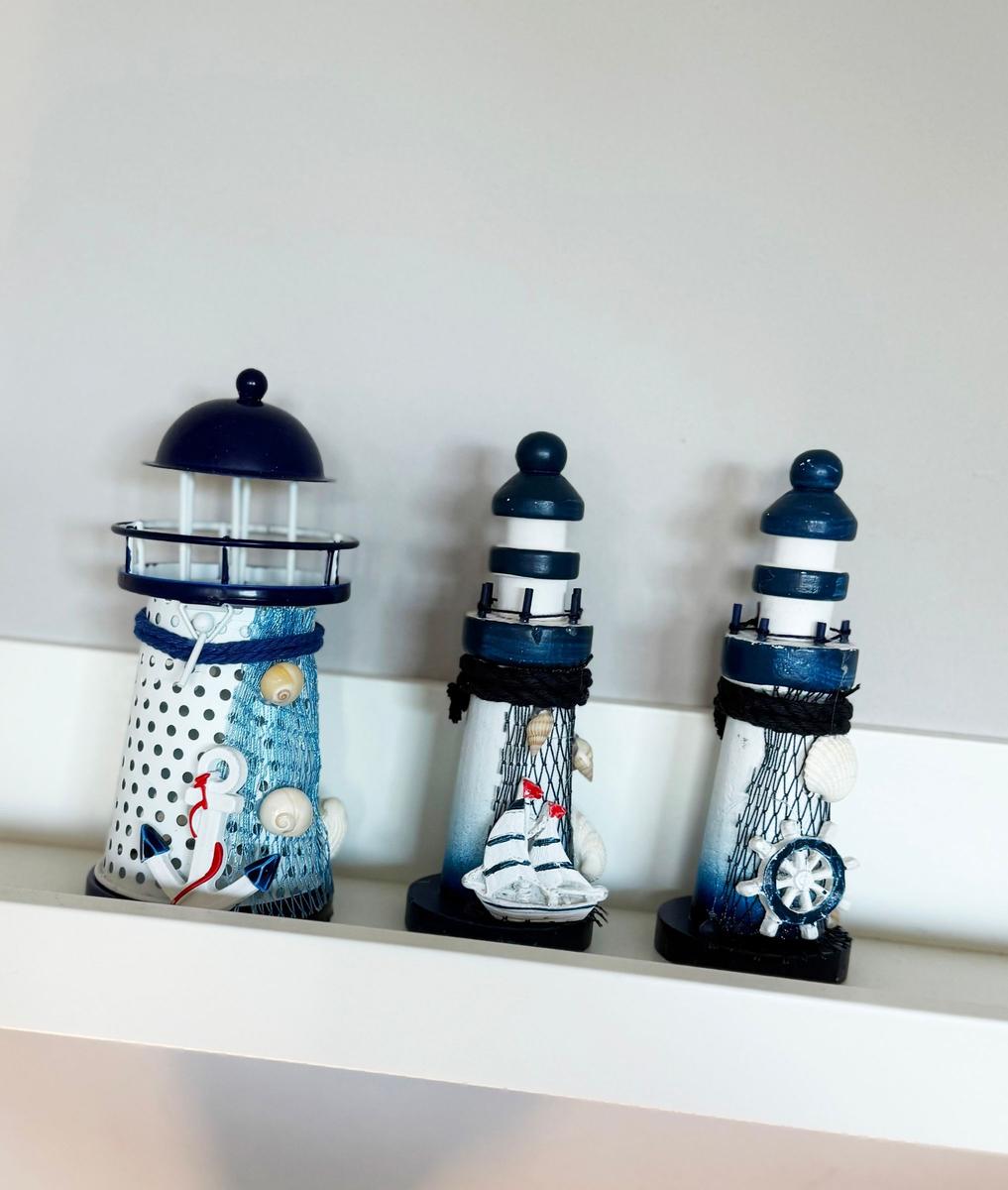 Drei dekorative Leuchttürme mit Seesternen und Ankern auf einem Regal.