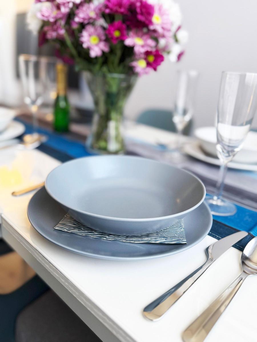 Tisch gedeckt mit grauen Tellern, Blumenvase und Gläsern.