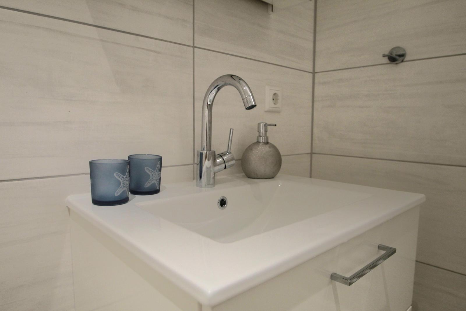 Waschbecken mit Wasserhahn, Seifenspender und zwei Gläsern mit Seesternmotiv.