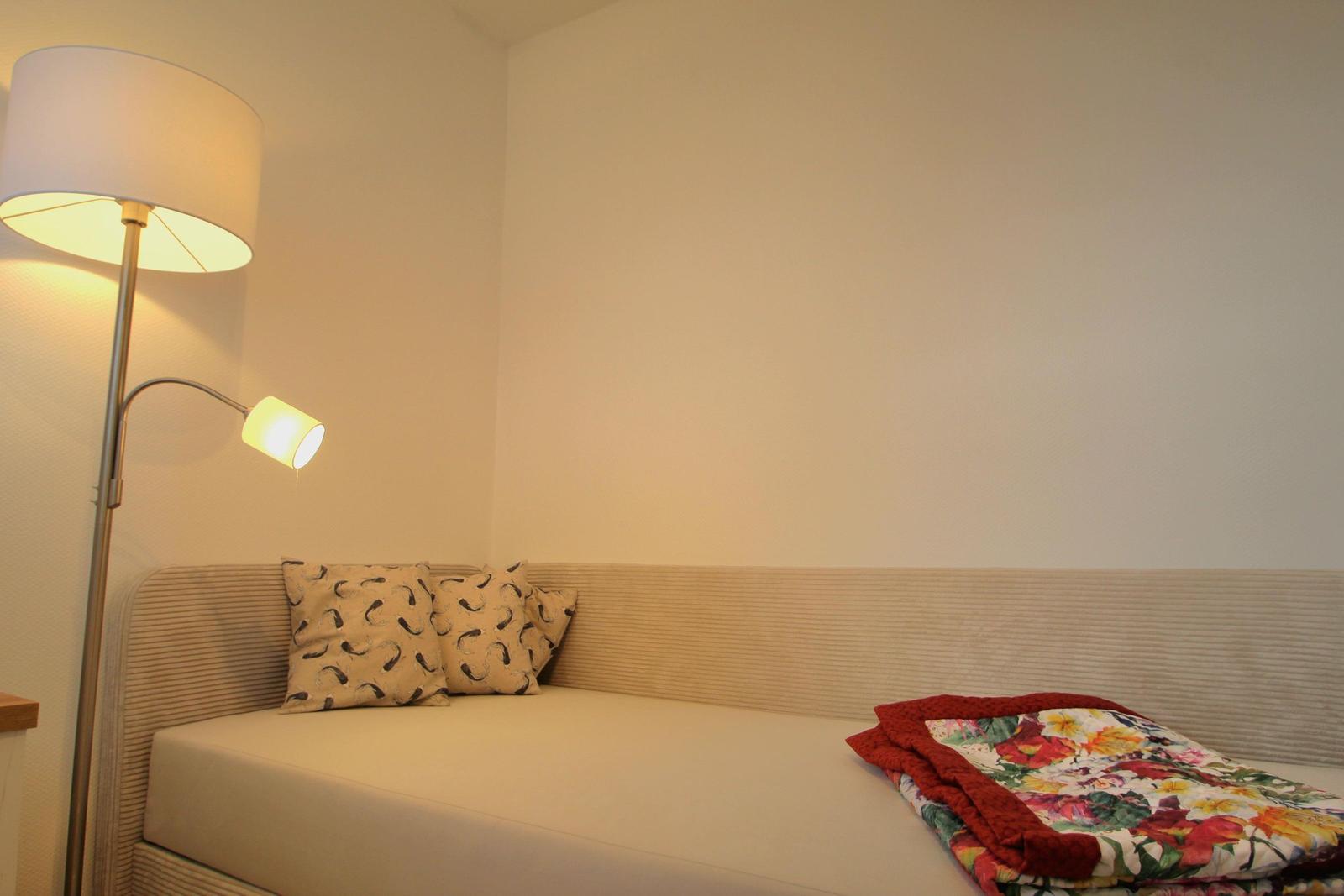 Schlafzimmer mit Bett, Kissen und Stehlampe.