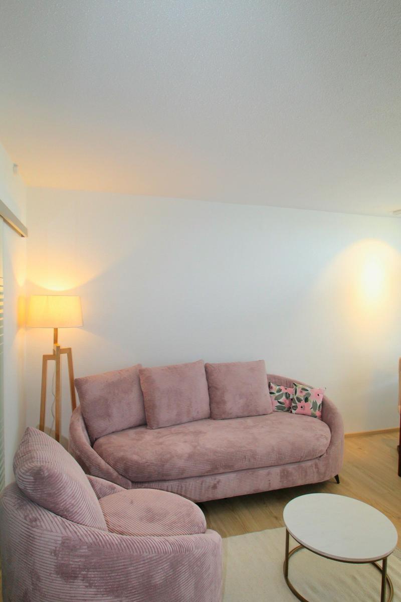 Ein Wohnzimmer mit rosa Sofa, Sessel und runder Tisch.
