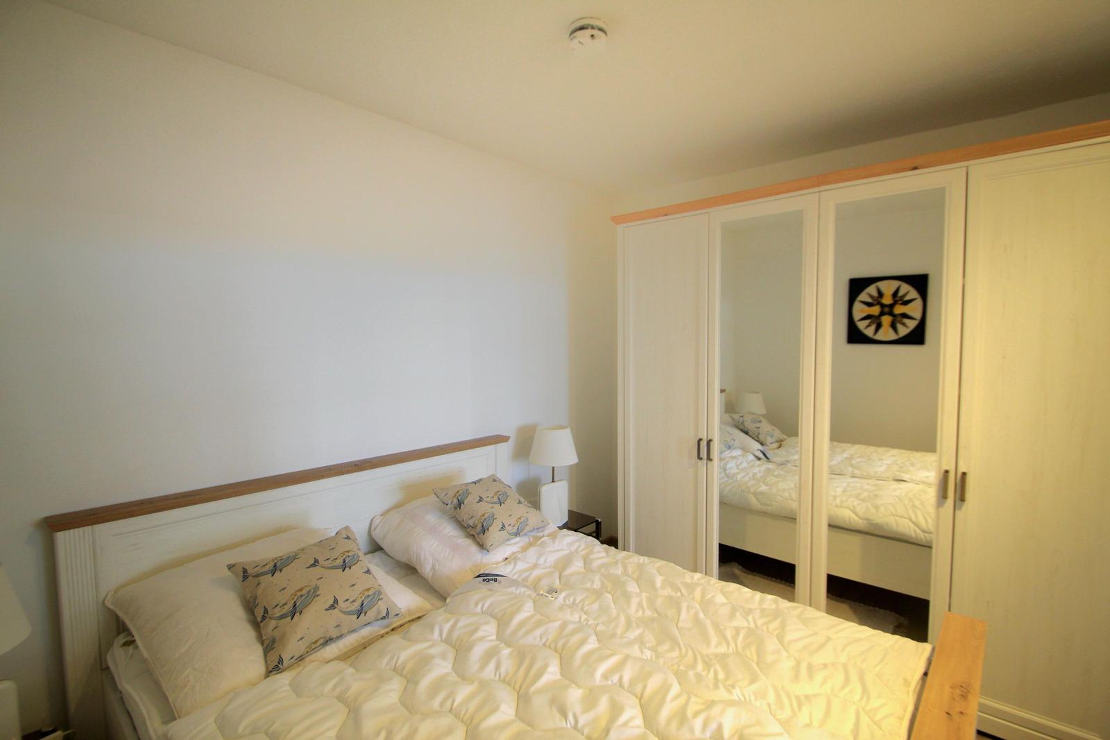 Schlafzimmer mit Doppelbett, Kleiderschrank mit Spiegeltüren und Nachttisch mit Lampe.