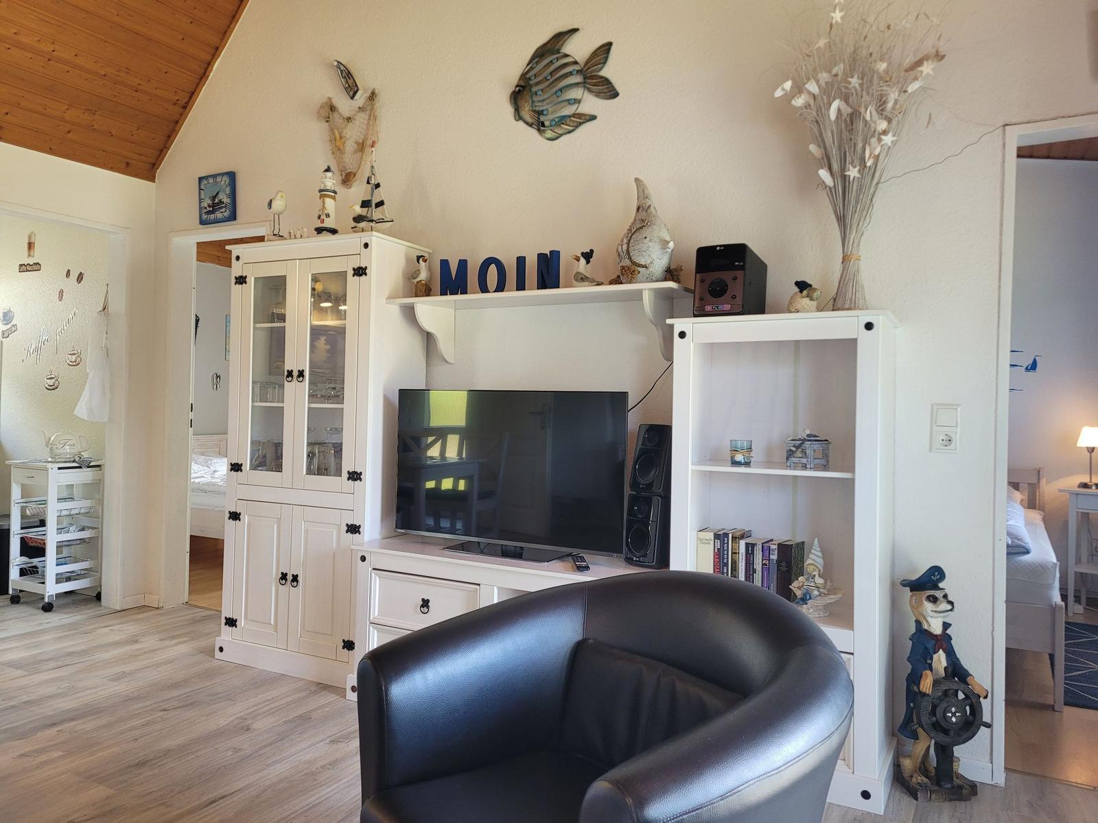 Wohnzimmer mit Fernseher, Schränken und Sitzgelegenheit. Sehenswert: Wanddekoration und Schiffsmotiv.
