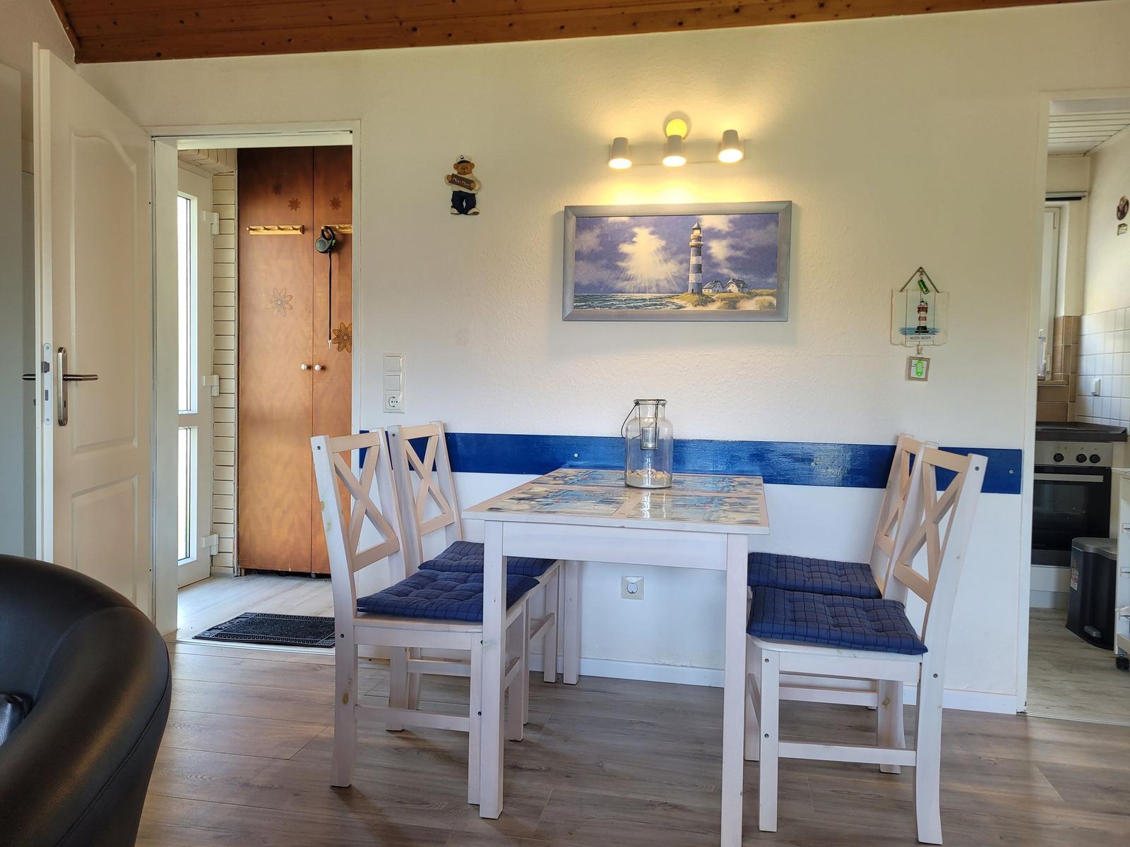 Essbereich mit Tisch, Stühlen und Wandbild. Durchgang zur Küche und Eingangstür.