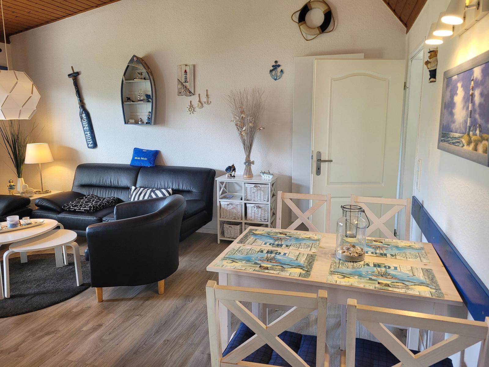 Wohn- und Essbereich mit Sofa, Tisch und Küchenzeile. Wanddekoration mit Segelbootmotiven.