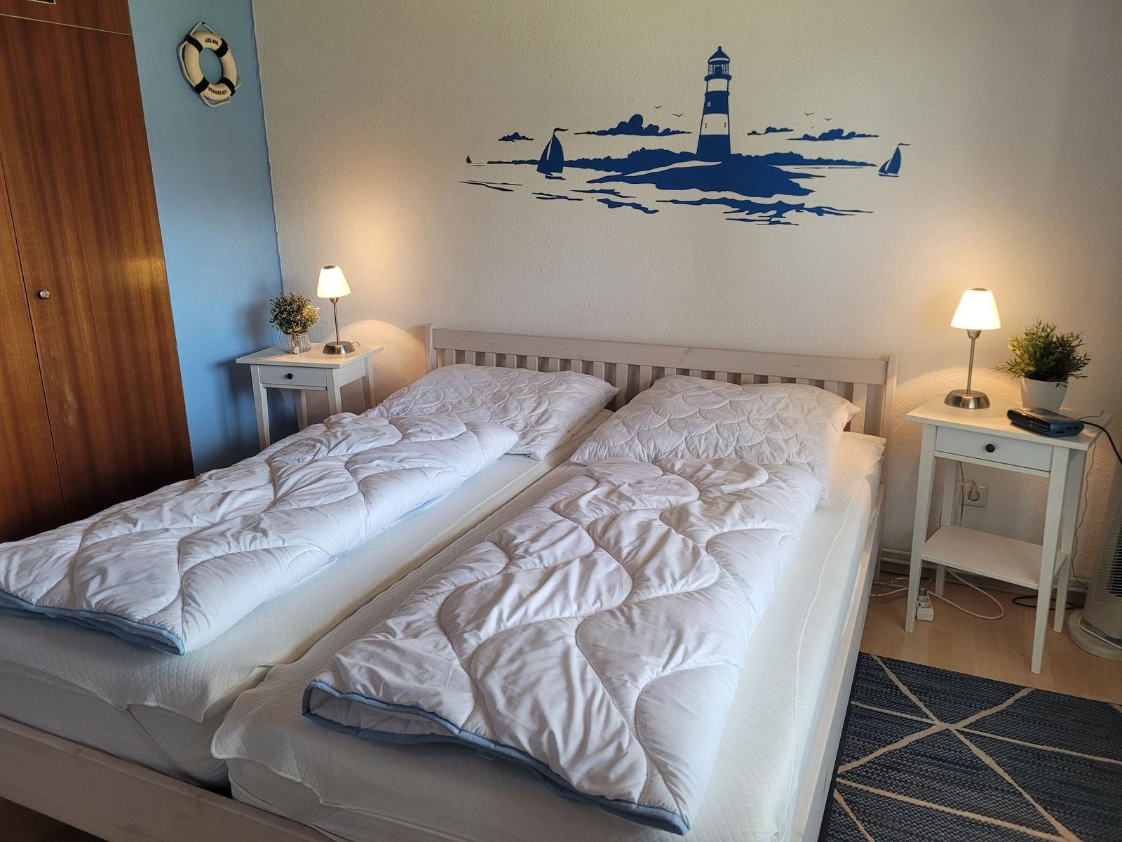 Schlafzimmer mit Doppelbett, zwei Nachttischen und Wandbild mit Leuchtturm.