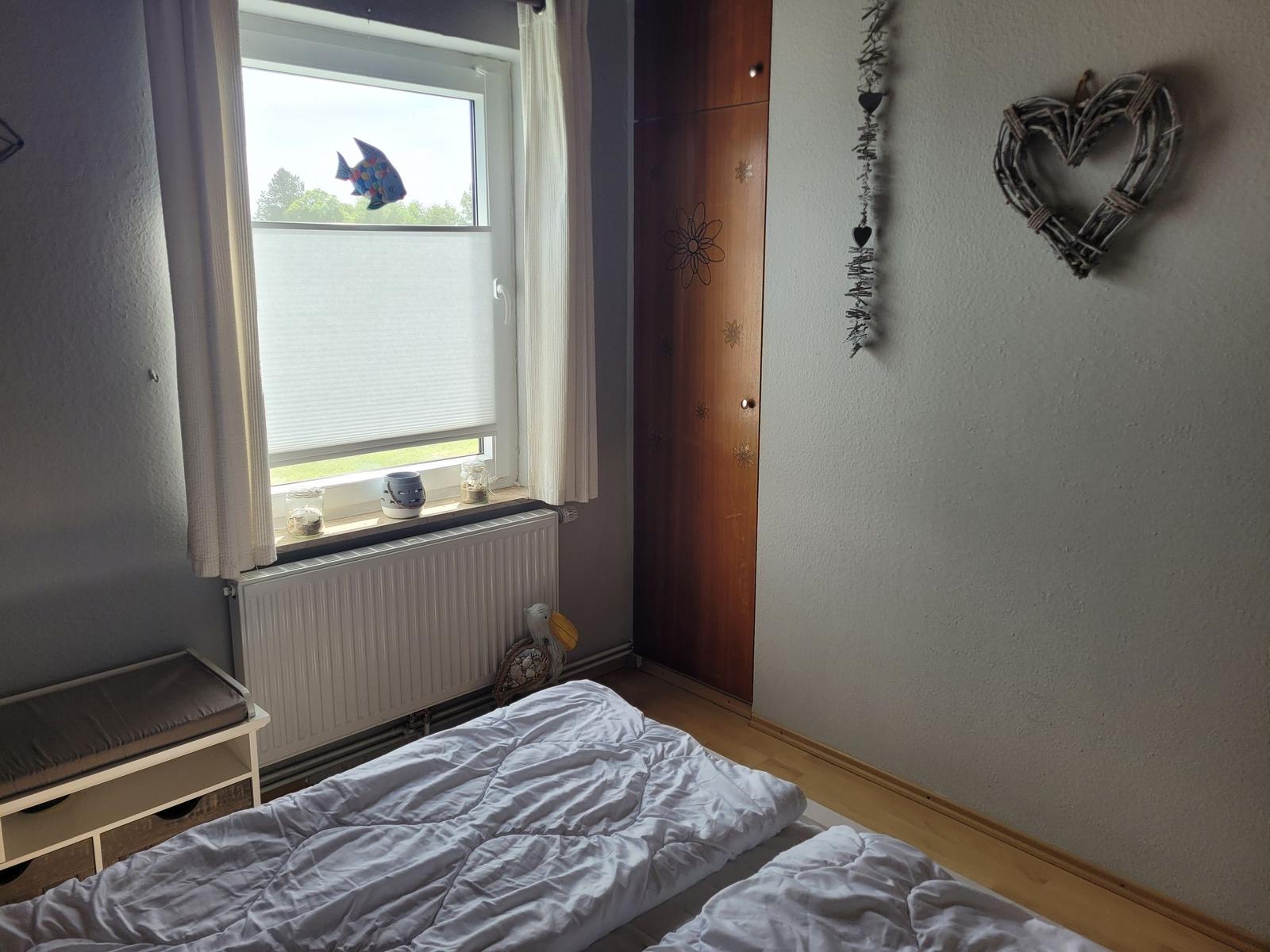 Schlafzimmer mit Bett, Fenster und Kleiderschrank.