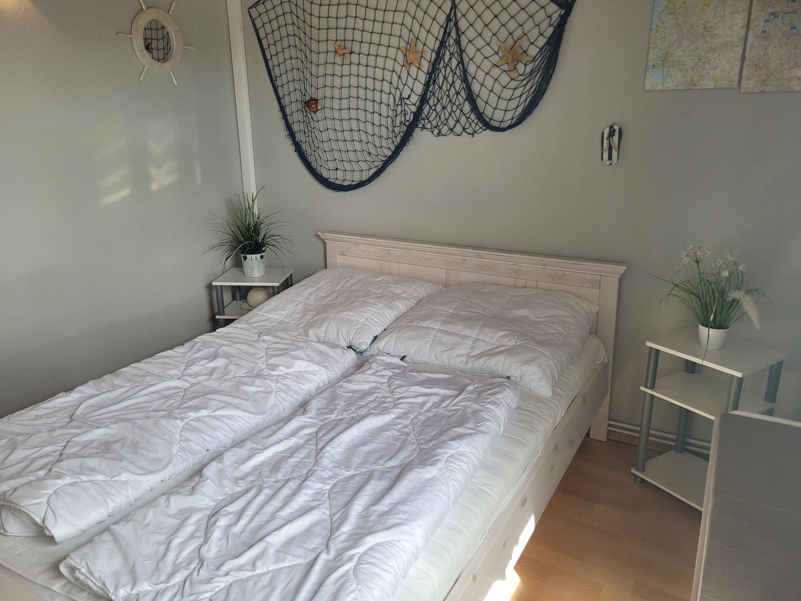 Schlafzimmer mit Bett, Nachttischen und maritimen Wanddekoration.