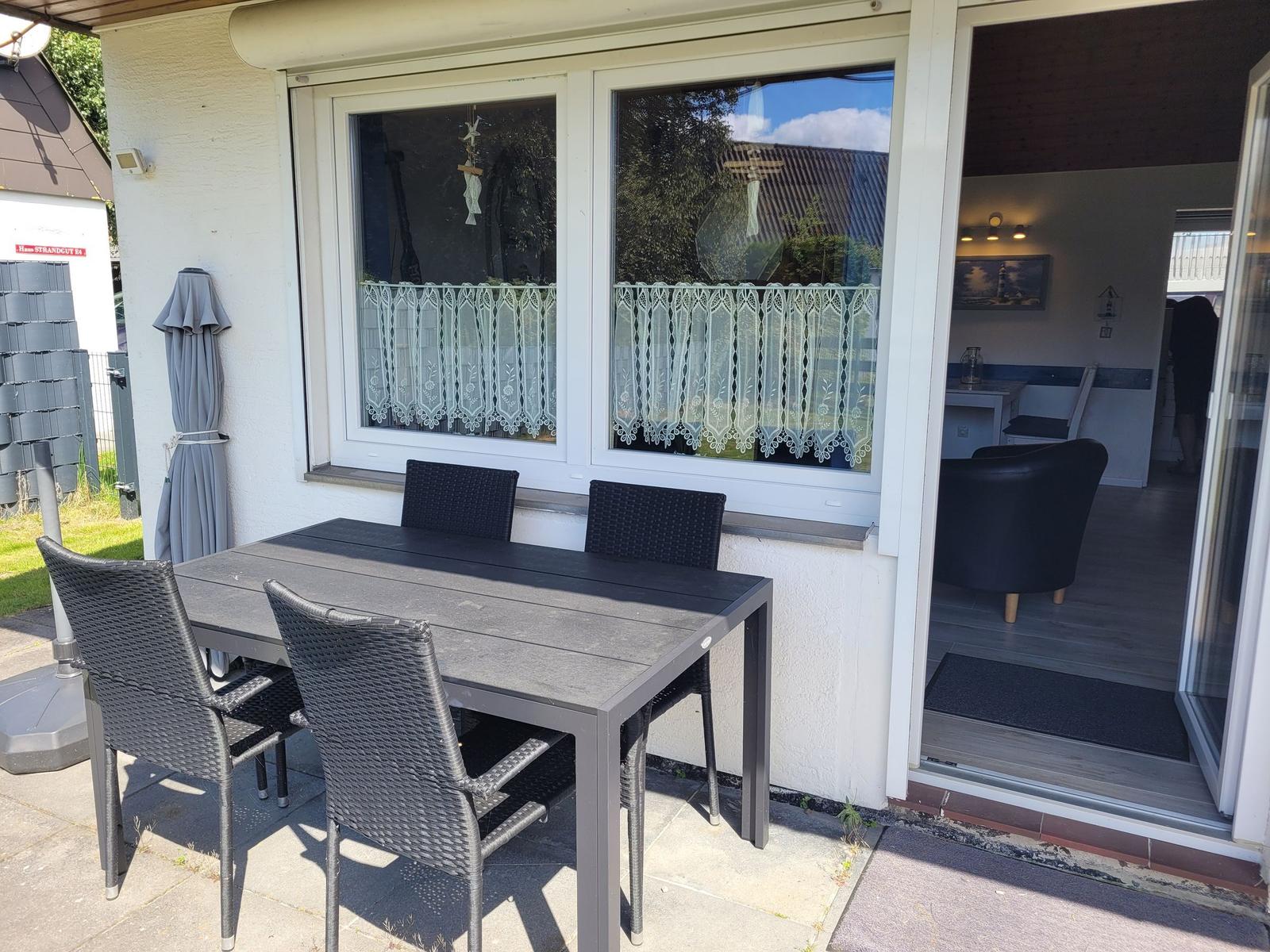 Terrasse mit Tisch und Stühlen, Schiebetür zum Innenraum mit Sitzgelegenheiten.