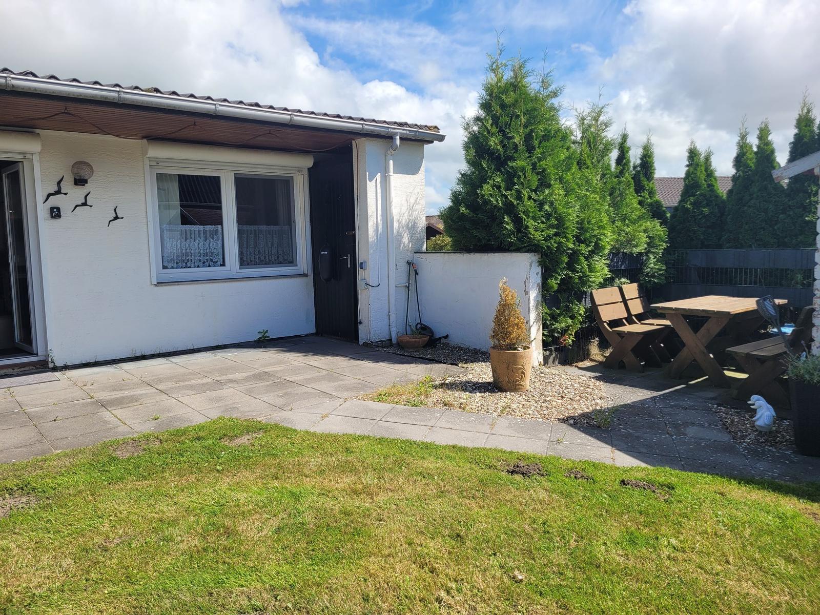 Hinterhof mit Terrasse, Garten und Holztisch mit Bänken.
