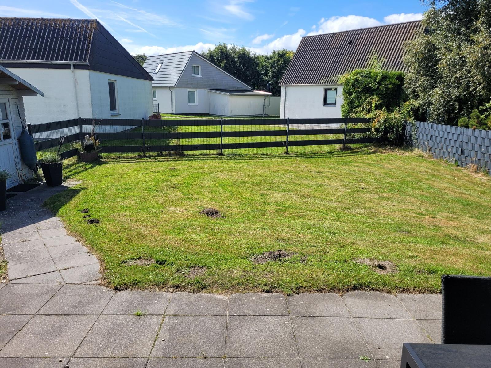 Garten mit Rasenfläche und Terrasse, umgeben von Zaun und Nachbarhäusern.